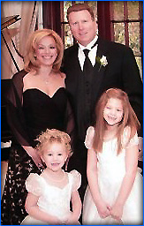 The image features a family posing together at a formal event  the father is wearing a tuxedo, the mother is dressed in evening wear, and there are three children in formal attire.