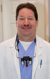 The image features a man wearing a white lab coat and stethoscope, standing in front of a wall with a hospital setting behind him. He has a beard and mustache, and is smiling at the camera.