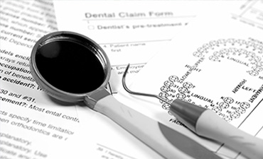 The image shows a pair of medical glasses with a magnifying glass placed on top of them, resting on a piece of paper which includes text related to dental care, specifically  dental claim form,  along with other printed information and a pen.