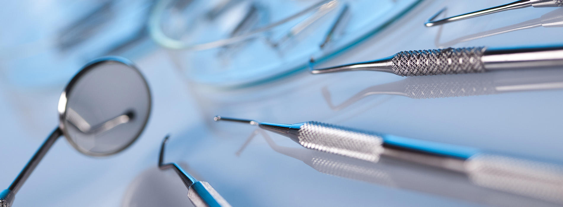 The image shows a close-up view of various surgical instruments, including needles and scissors, with a focus on their sharp edges and metallic surfaces, set against a blurred background that suggests a medical or sterile environment.