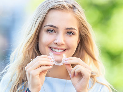 The image shows a smiling woman holding a toothbrush with toothpaste on its bristles.