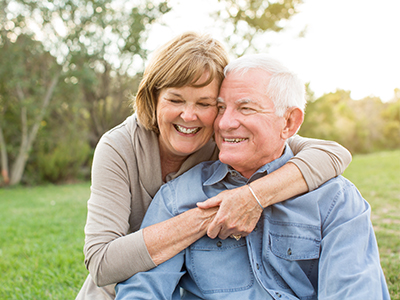 An older couple embracing each other outdoors during daylight.