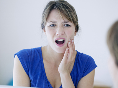 A woman with her mouth open, making an expression that suggests she might be screaming or yelling, while looking at her own reflection in a mirror.