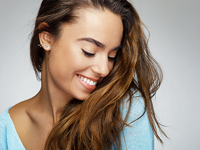 A smiling woman with long hair, wearing a light blue top, looking slightly away from the camera.