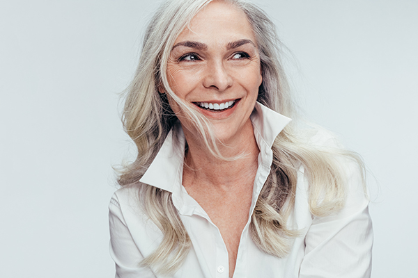 A woman with short hair is smiling at the camera, wearing a white shirt and has blonde hair.