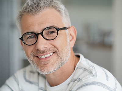 The image features a man with glasses smiling at the camera. He has short hair and appears to be indoors, possibly in an office setting.