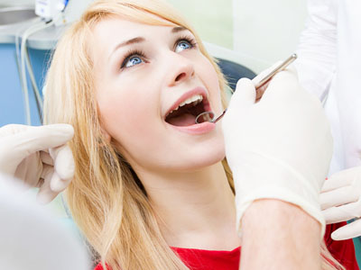 A woman undergoing dental treatment with her mouth open while wearing a surgical mask.