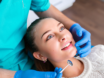 A woman receiving dental care from a dentist using a dental mirror and probe.