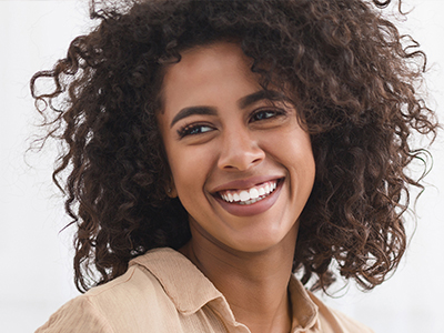 A woman with curly hair is smiling and looking off to the side.